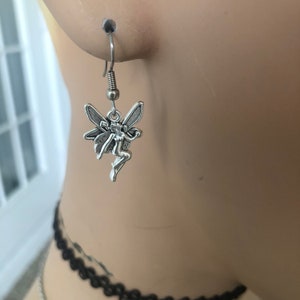 May include: Silver fairy dangle earrings with a detailed design. The fairy is depicted with wings outstretched and a flowing dress.