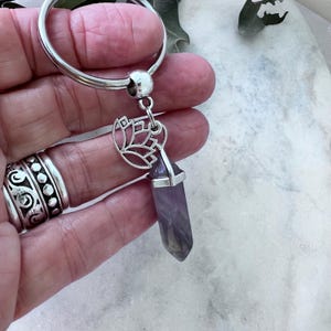 May include: A silver key chain with a purple crystal charm and a silver lotus flower pendant.