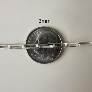 May include: Close-up of a silver chain with a 3mm width, measured against a US dime coin. The chain is made of linked rectangular pieces.