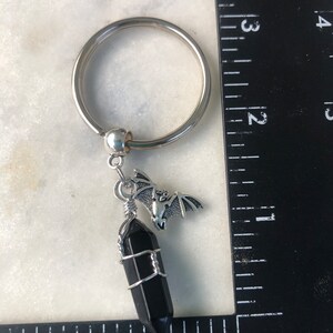 May include: A silver key chain with a black crystal charm and a silver bat charm.
