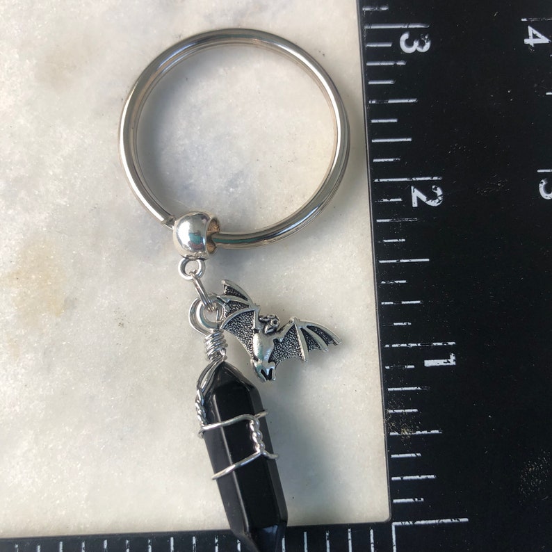 May include: A silver key chain with a black crystal charm and a silver bat charm.