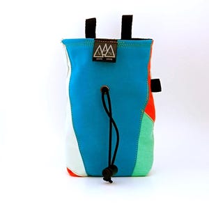 Peut inclure: Un sac à magnésie avec un panneau avant bleu vif, un panneau latéral blanc et des accents orange et vert. Il comprend une fermeture à cordon noir avec un stoppeur, deux boucles supérieures noires et une étiquette noire avec le texte blanc Picos Climb.