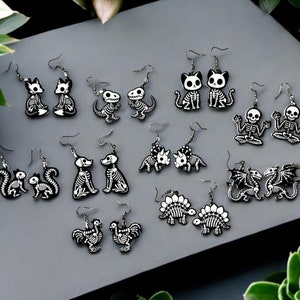 Puede incluir: Un conjunto de 10 pares de pendientes de esqueleto con varios dise&ntilde;os de animales, incluyendo gatos, zorros, ardillas, dinosaurios, perros, dragones y un gallo. Los pendientes est&aacute;n hechos de acr&iacute;lico blanco y negro y son perfectos para agregar un toque de fantas&iacute;a a cualquier atuendo.