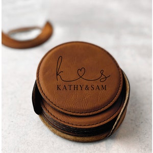 May include: Set of six brown leather coasters with a personalized design. The top coaster features the initials "K & S" with a heart and the text "Kathy & Sam".