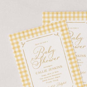 K&ouml;nnte beinhalten: Zwei Babyparty-Einladungen mit einem gelb-wei&szlig; karierten Rand. Die Einladungen zeigen eine elegante goldene Schrift, die "Baby Shower" lautet, und enthalten Details wie den Namen der Geehrten, Datum, Uhrzeit und Ort.