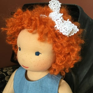 May include: A handmade doll with red curly hair, blue eyes, and a white lace headband. The doll is wearing a blue denim dress with white lace trim.