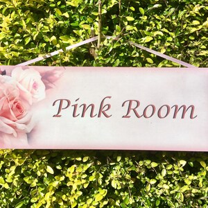 May include: Pink room sign with a pink background and a floral design featuring pink roses. The sign reads "Pink Room" in a cursive font.