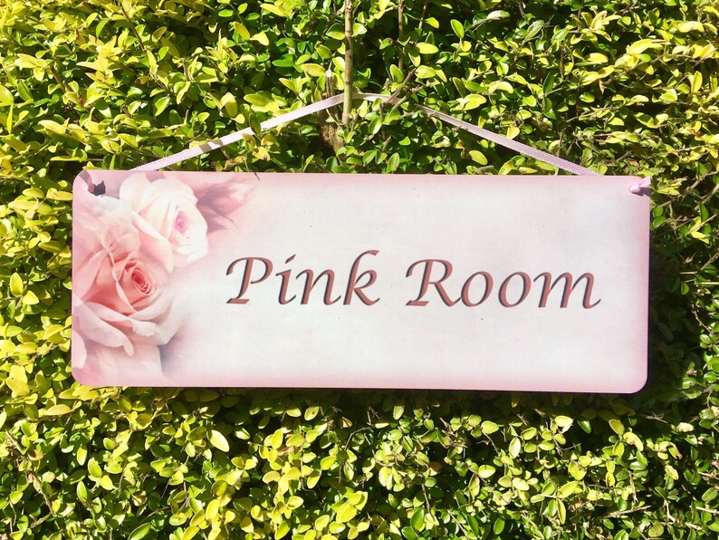 May include: Pink room sign with a pink background and a floral design featuring pink roses. The sign reads "Pink Room" in a cursive font.