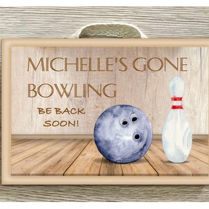 May include: Watercolor-style sign with a bowling theme. The sign reads "MICHELLE'S GONE BOWLING BE BACK SOON!" and features a blue bowling ball and a white bowling pin with red stripes. The background is wood-textured.