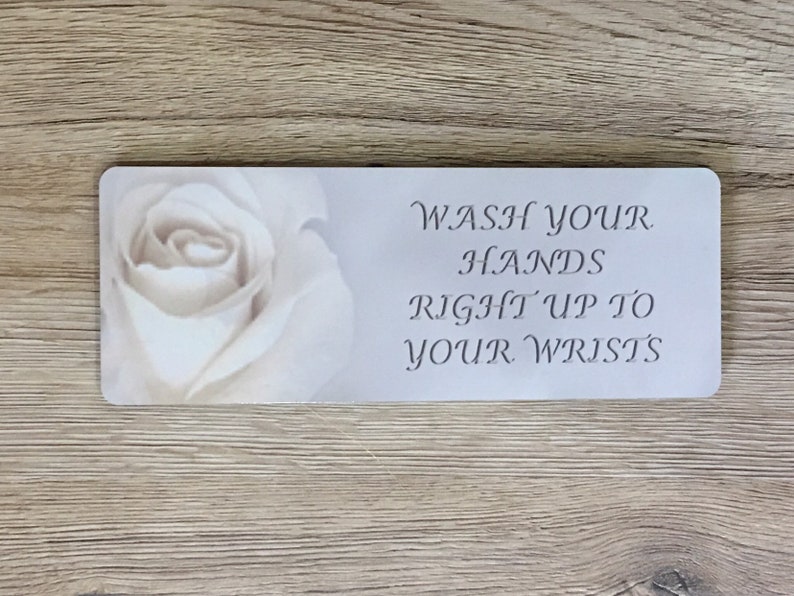 May include: White sign with a white rose image and the text "WASH YOUR HANDS RIGHT UP TO YOUR WRISTS".