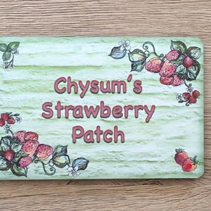 May include: A green wooden sign with a whitewashed finish and a strawberry theme. The sign reads "Chysum's Strawberry Patch" in pink lettering.