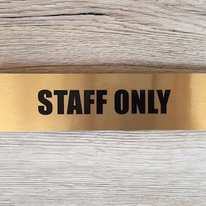 May include: A gold metal sign with black text that reads "STAFF ONLY".