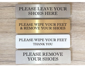 May include: Four silver and gold signs with black text. The signs read: "Please leave your shoes here", "Please wipe your feet & remove your shoes", "Please wipe your feet thank you", and "Please remove your shoes".