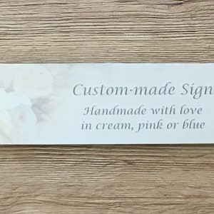May include: A white sign with a floral design and the text "Custom-made Sign Handmade with love in cream, pink or blue".