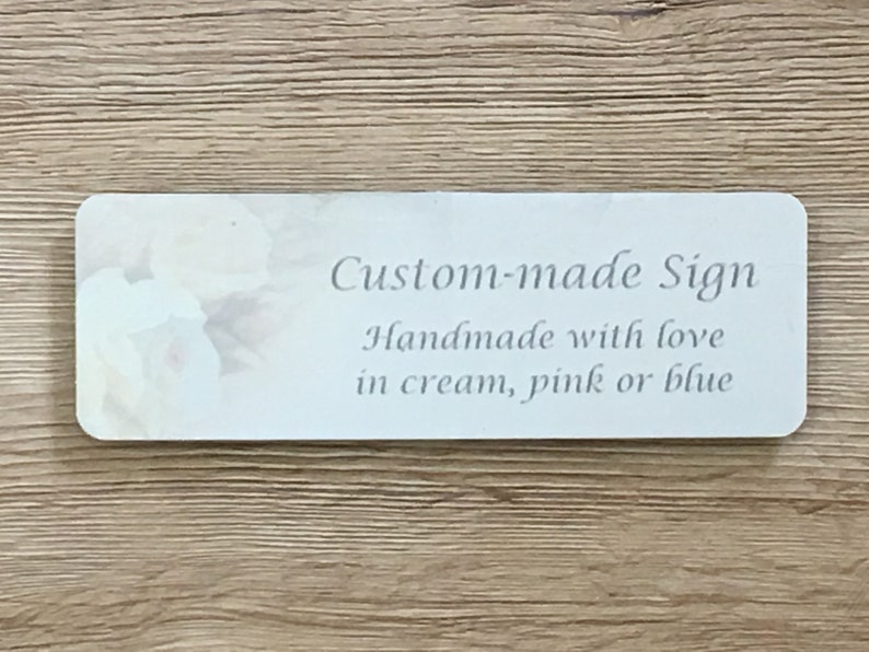 May include: A white sign with a floral design and the text "Custom-made Sign Handmade with love in cream, pink or blue".
