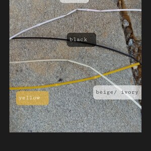 May include: Image showing thin, colored cords labeled with the colors white, black, yellow, and beige/ivory. The cords are laid out on a textured, gray surface. The word "white" is in a white rectangle.