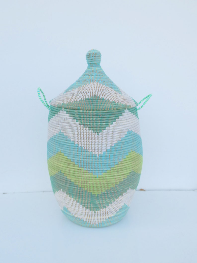 May include: A woven storage basket with a lid, featuring a geometric pattern in shades of green, blue, and white. The basket has two handles on the lid.