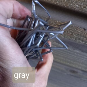 May include: A bundle of gray metal star-shaped objects. The objects are held in a hand, with the word "gray" in a light brown box in the lower left corner. The background is a wooden surface.