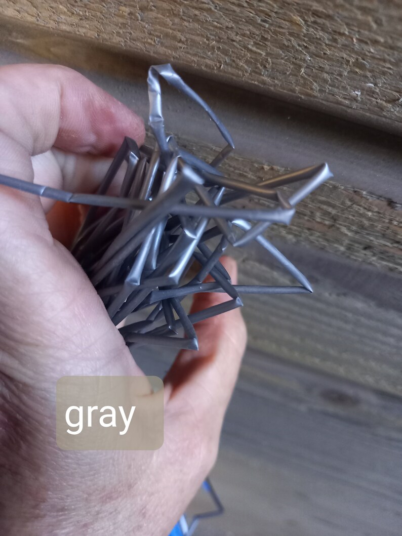 May include: A bundle of gray metal star-shaped objects. The objects are held in a hand, with the word "gray" in a light brown box in the lower left corner. The background is a wooden surface.