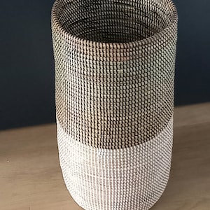 May include: A woven basket with a natural brown top and a white bottom. The basket is cylindrical in shape and has a woven pattern.