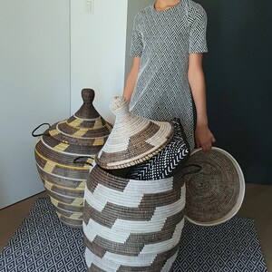 May include: Woven storage baskets in various sizes and patterns. The largest basket is open, revealing smaller baskets and a lid. The baskets are brown, white, and yellow. The scene is set on a patterned rug.