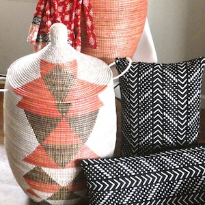 May include: Two black and white patterned throw pillows and a large, woven, pink and white storage basket with a geometric pattern.