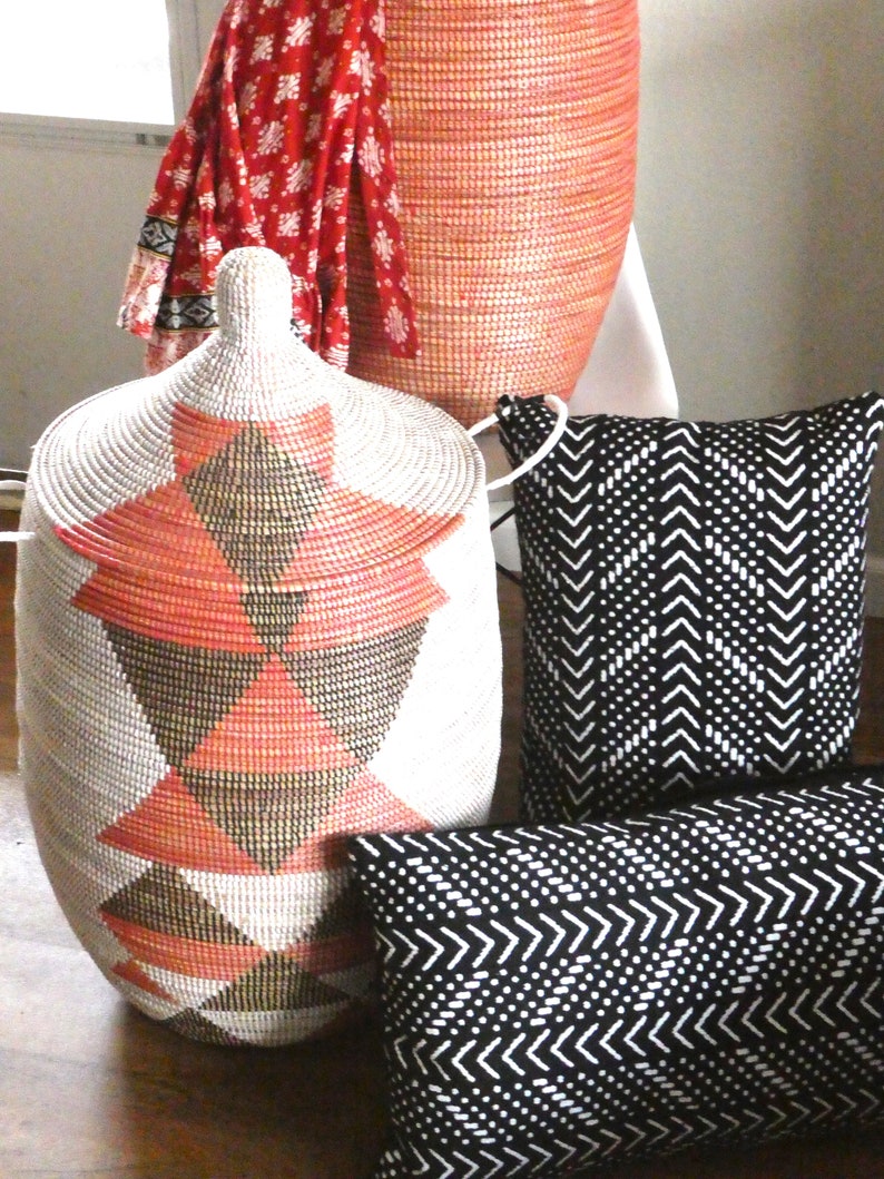 May include: Two black and white patterned throw pillows and a large, woven, pink and white storage basket with a geometric pattern.