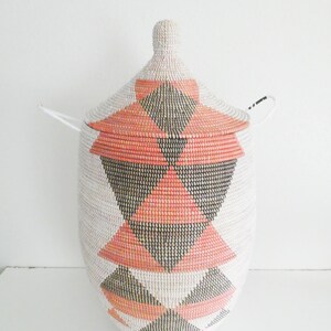 May include: A large, white woven basket with a lid. The basket has a geometric pattern of pink and black triangles.