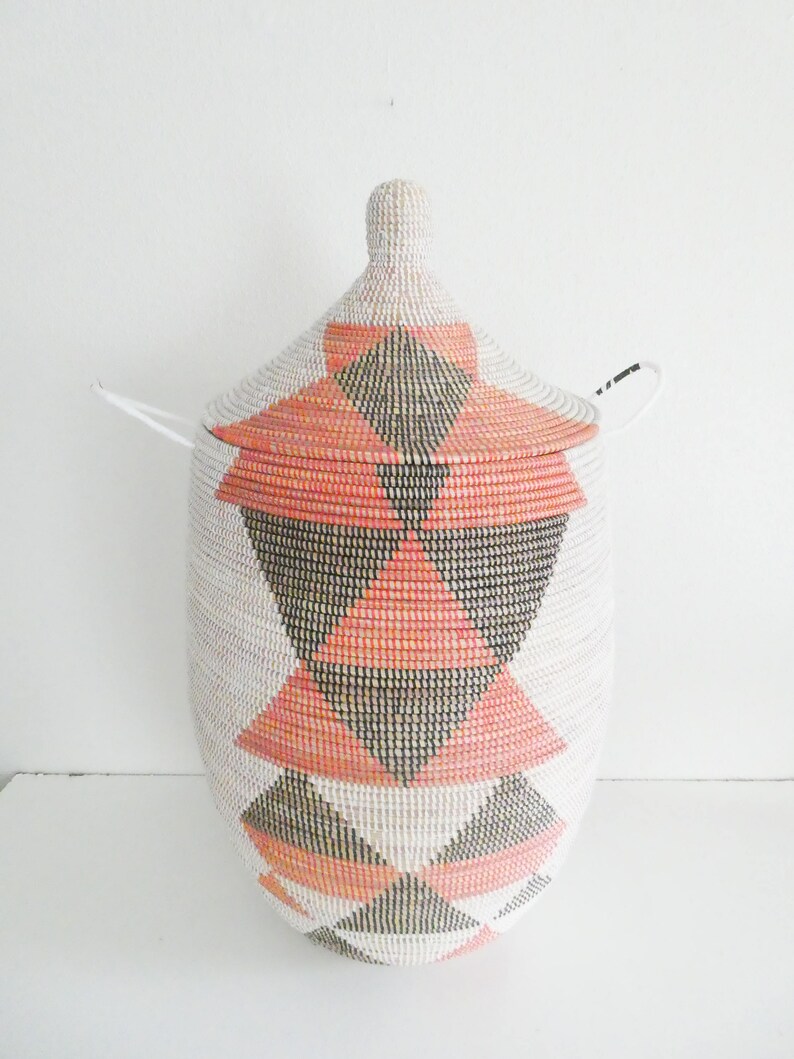 May include: A large, white woven basket with a lid. The basket has a geometric pattern of pink and black triangles.
