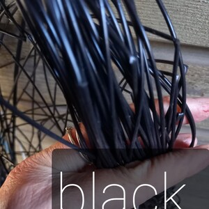 May include: A bundle of black wire held in a hand, with the word "black" overlaid on the image. The wire appears to be tightly wound and is a solid, glossy black color. The background is a wooden surface.