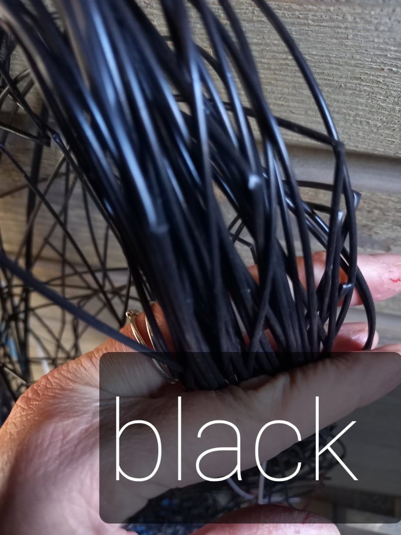 May include: A bundle of black wire held in a hand, with the word "black" overlaid on the image. The wire appears to be tightly wound and is a solid, glossy black color. The background is a wooden surface.