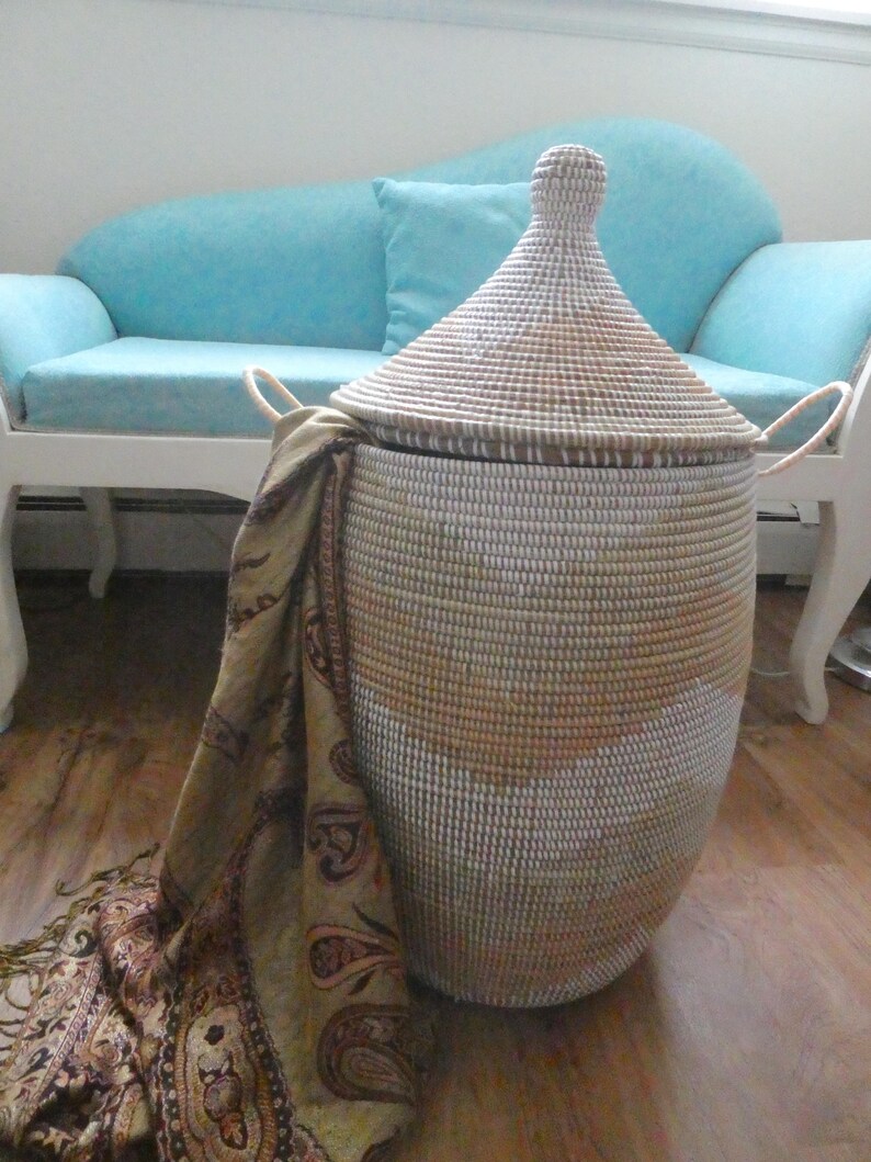 May include: A white and brown woven storage basket with a lid and handles. The basket is sitting on a wooden floor next to a light blue couch.