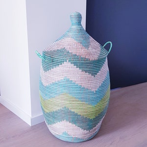 May include: A large, woven storage basket with a lid. The basket is made of natural materials and has a blue, green, and white geometric pattern.