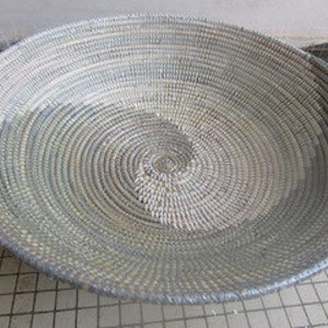 May include: A large, round, woven basket with a natural, light brown color on one side and a darker, gray color on the other side. The basket is made of natural materials and has a unique, hand-woven design.