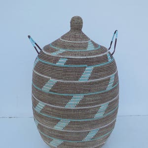 May include: A large, woven storage basket with a lid and two handles. The basket is brown with white and light blue stripes.