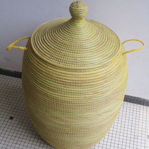 May include: A large, yellow woven storage basket with a lid and two handles. The basket is made of natural materials and has a traditional design.