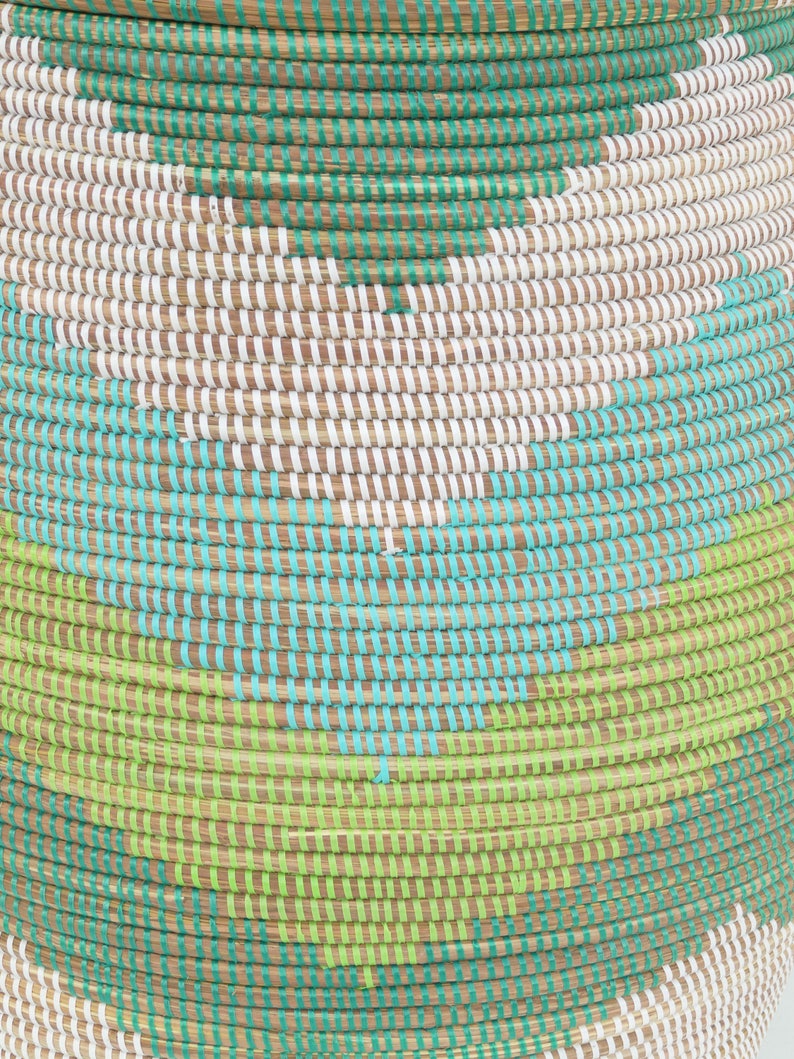 May include: A woven basket with a geometric pattern in shades of green, blue, and white. The basket is made of natural materials and has a round shape.