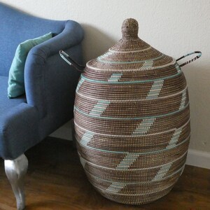 May include: A large, brown and white woven storage basket with a lid and handles. The basket has a geometric pattern of stripes and is made of natural materials.