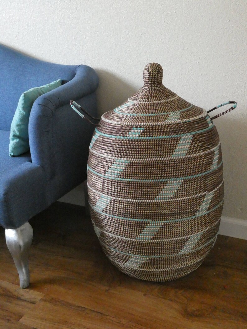 May include: A large, brown and white woven storage basket with a lid and handles. The basket has a geometric pattern of stripes and is made of natural materials.