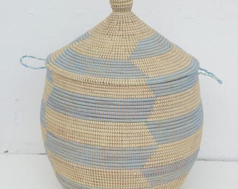 May include: A large, woven storage basket with a lid. The basket is made of natural materials and has a blue and white striped pattern. The lid has a rounded top.