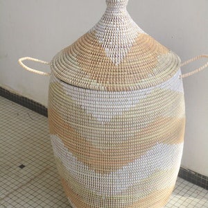 May include: A large, woven storage basket with a lid. The basket is made of natural materials and has a white and tan geometric pattern. The lid has a pointed top.