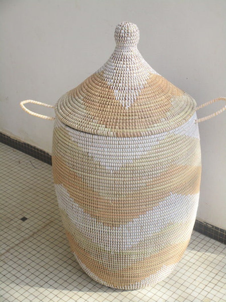 May include: A large, woven storage basket with a lid. The basket is made of natural materials and has a white and tan geometric pattern. The lid has a pointed top.