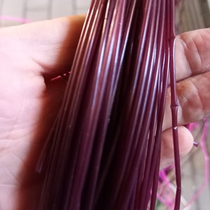 May include: A bundle of deep purple plastic cord, held in a hand. The cord is smooth and shiny.