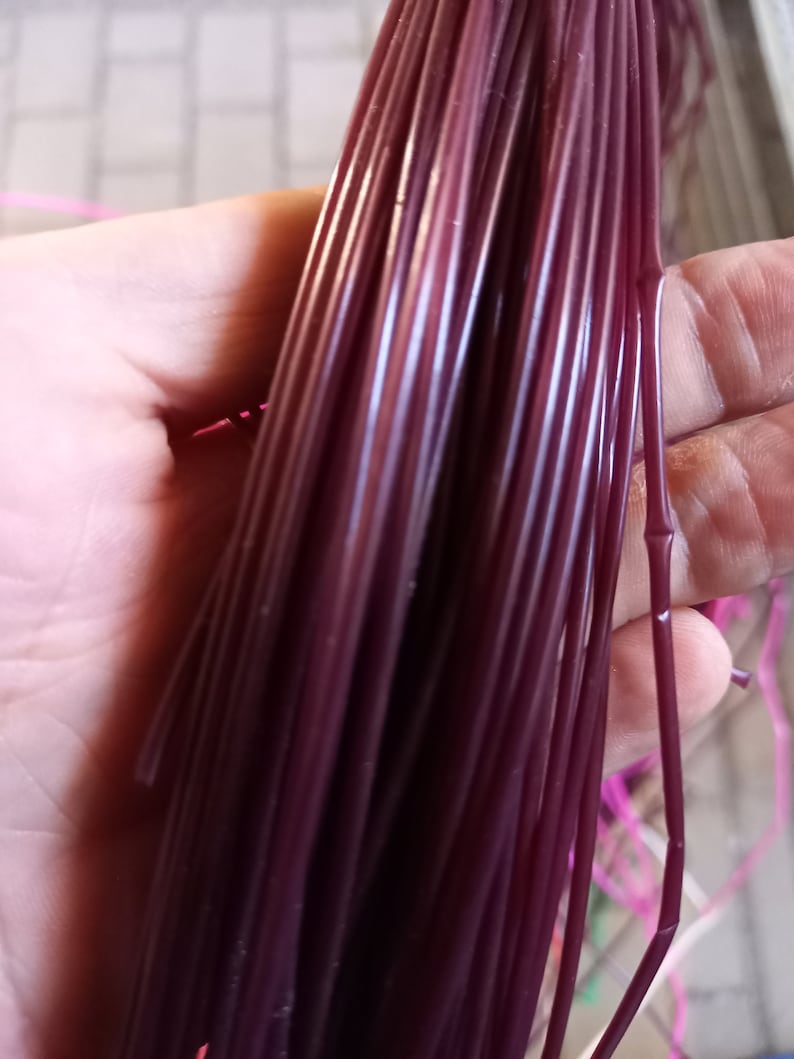 May include: A bundle of deep purple plastic cord, held in a hand. The cord is smooth and shiny.