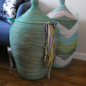 May include: Two large woven storage baskets with lids. The basket on the left is teal green and the basket on the right is white, green, and blue.