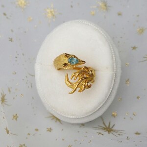 May include: A gold ring with a fox design and a blue gemstone. The ring is in a white velvet ring box.
