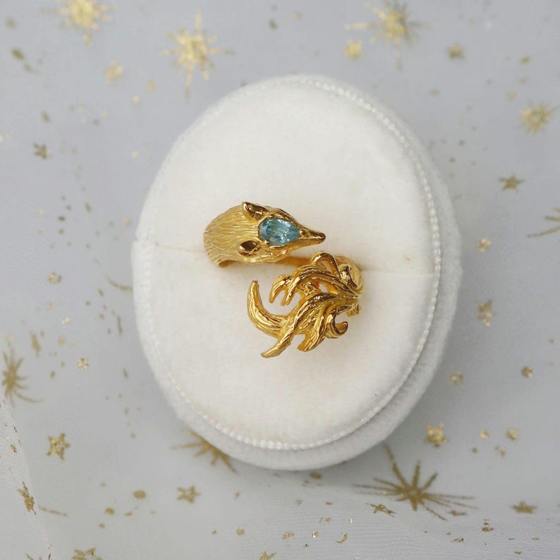 May include: A gold ring with a fox design and a blue gemstone. The ring is in a white velvet ring box.
