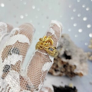 May include: A gold-tone ring featuring a detailed design of a bird with a multi-colored gemstone eye.