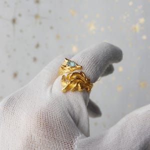 May include: A gold ring with a fox design and a blue gemstone in the eye. The ring is on a white surface.