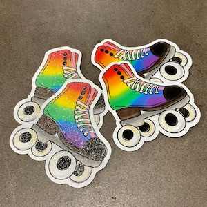 May include: Three rainbow roller skate stickers with glitter accents. The skates have black wheels and white laces.
